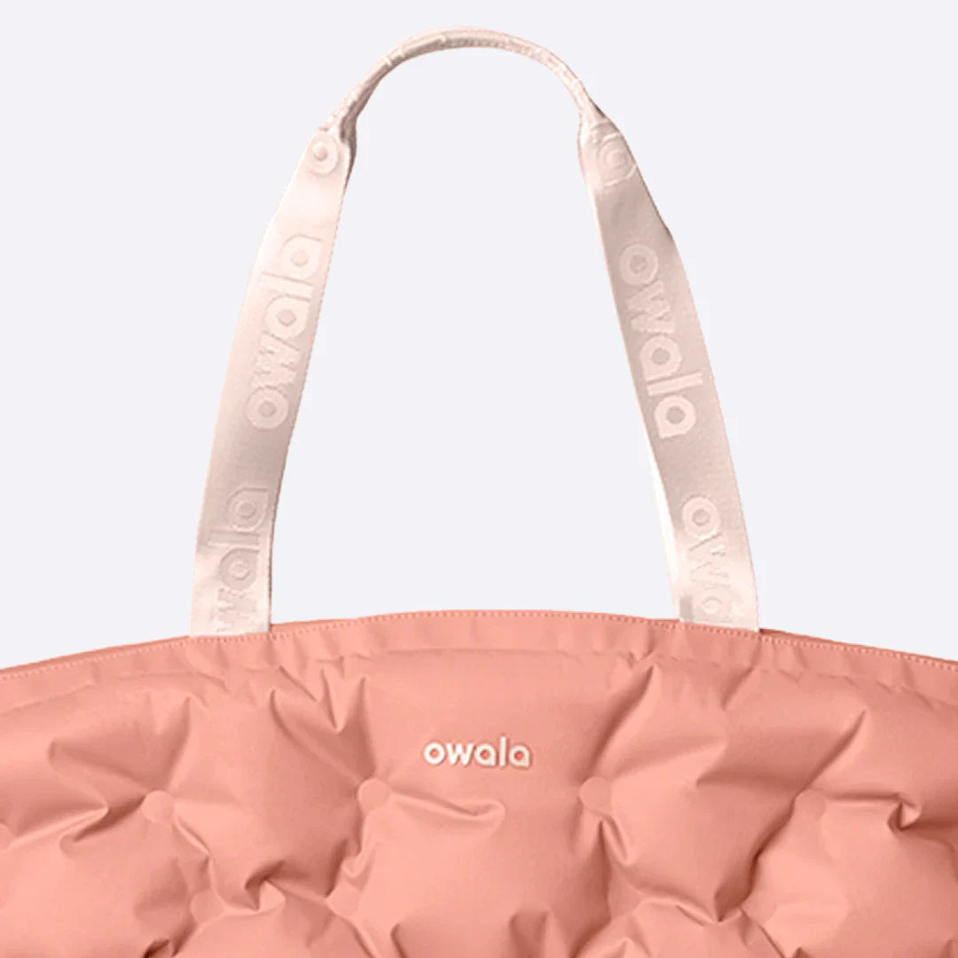 Close-up of the Owala Cloud Insulated Tote in Rosewood, peach pink pillowed body with cream owala-tape handles featuring repeating Owala logo and cream Owala logo on the body
